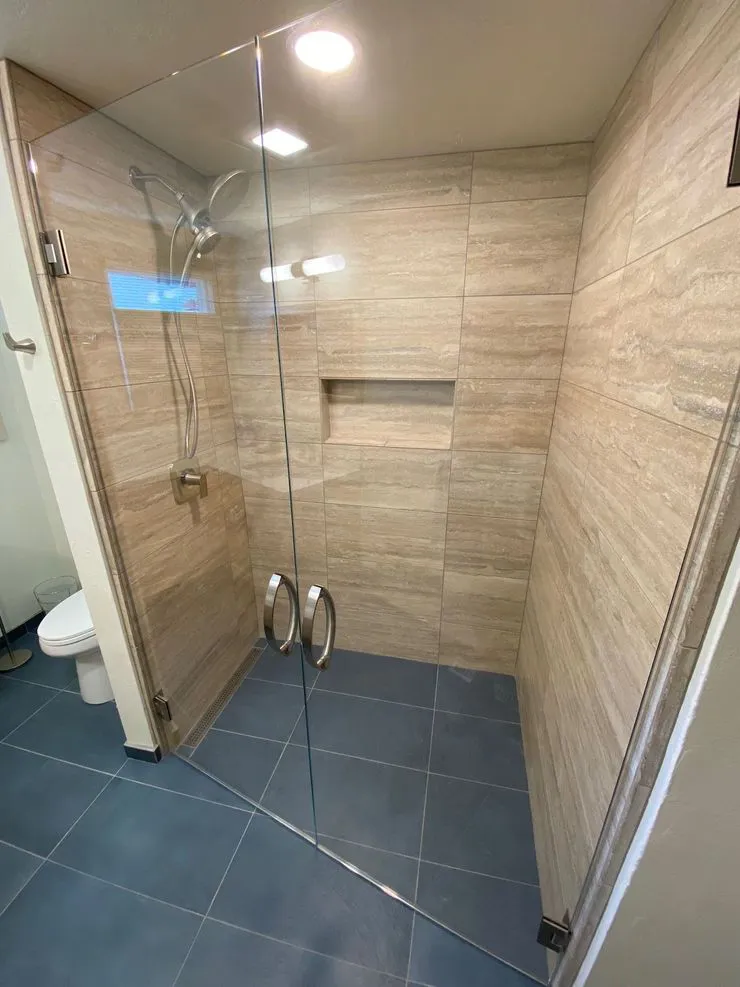 A modern shower with beige tile walls and a glass door, featuring a built-in shelf and sleek fixtures, designed by Labourdette Construction in Sebastopol.
