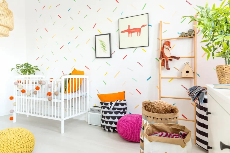 A brightly decorated nursery featuring a white crib, colorful wall designs, a knitted pouf, and assorted toys and decorative items.