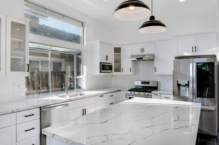 A modern kitchen designed by Lemon Remodeling in San Jose, featuring white cabinetry, marble countertops, stainless steel appliances, and pendant lighting.