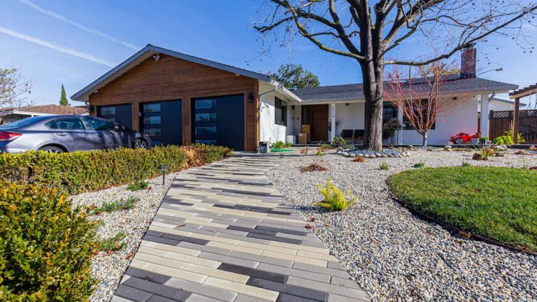 A modern house exterior in San Jose featuring a sleek walkway, a wooden garage, a white facade, and minimalist landscaping with gravel and plants, completed by Lemon Remodeling.