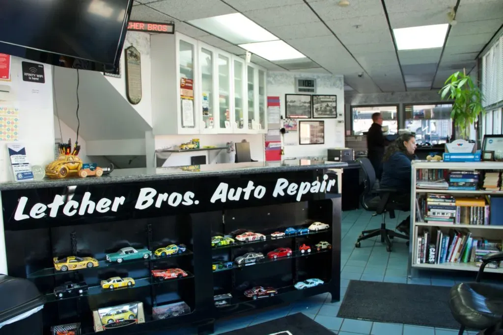 Interior of Letcher Brothers Auto Repair in Pinole featuring a counter with model cars, a busy office environment, and a bookshelf with manuals.
