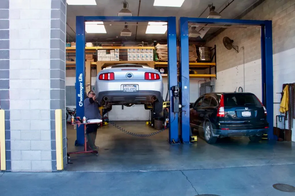 "Inside Letcher Brothers Auto Repair in Pinole, a mechanic works on a car elevated on a hydraulic lift in a well-organized garage."