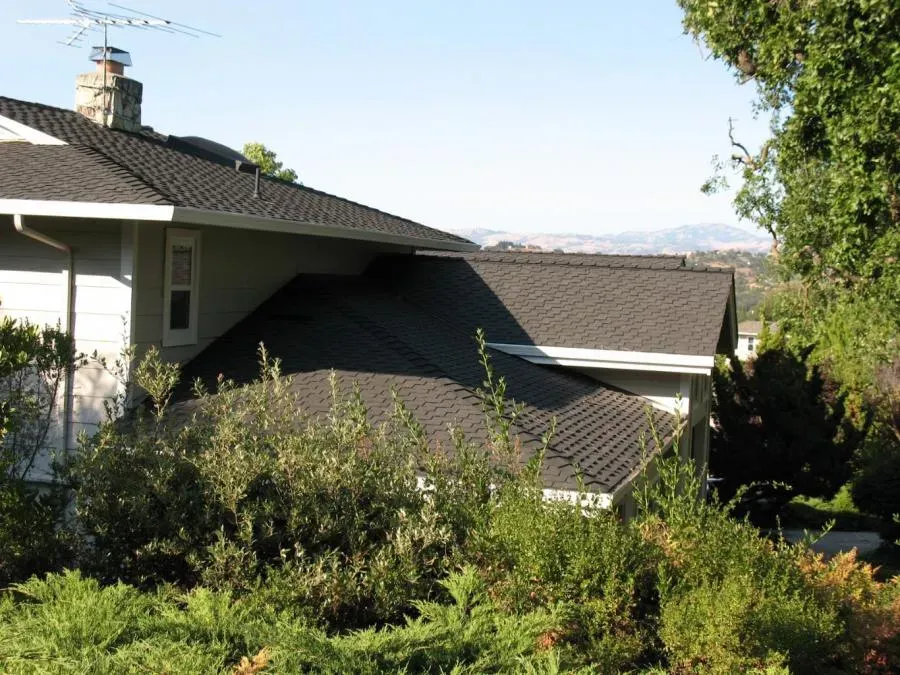 A house in San Jose with a newly installed roof by Los Gatos Roofing, surrounded by trees and overlooking a distant landscape.