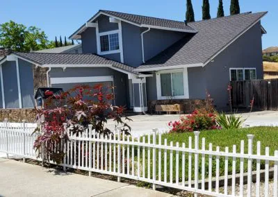 A modern two-story house with a newly installed gray roof by Los Gatos Roofing, located in San Jose, with a white picket fence and a well-maintained garden.