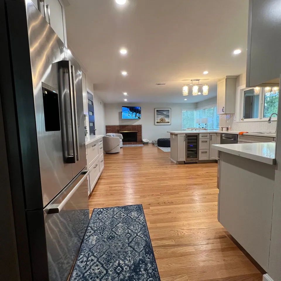 An open-concept kitchen with stainless steel appliances, a hardwood floor, and modern white cabinetry, showcasing the renovation work of Make It Right Carpentry, Inc in Novato.
