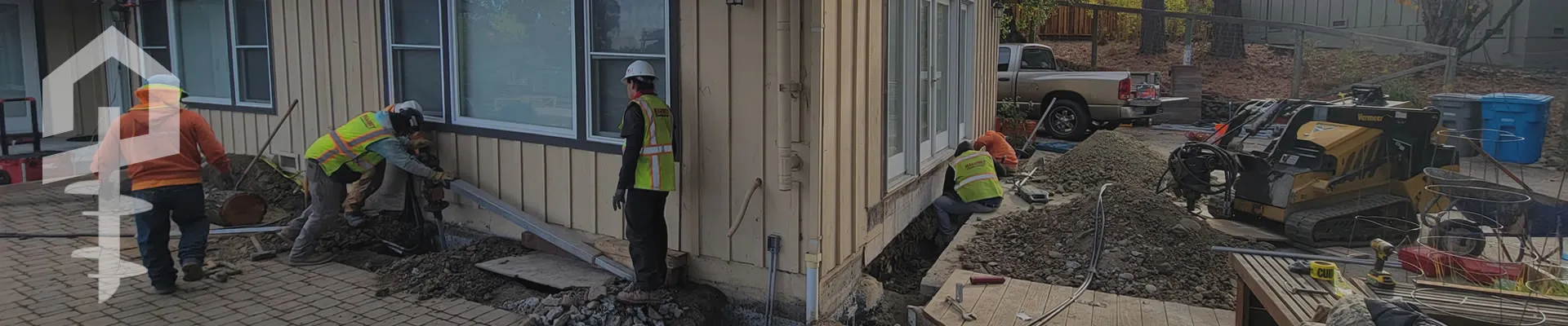 Construction workers from Maloney Construction, Inc. reinforcing a building foundation in Novato, with machinery and tools visible on site.