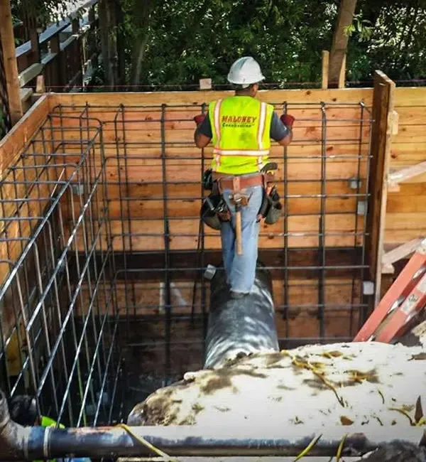 A construction worker from Maloney Construction, Inc. wearing a safety vest and helmet inspects rebar reinforcements inside a wooden structure at a construction site in Novato.