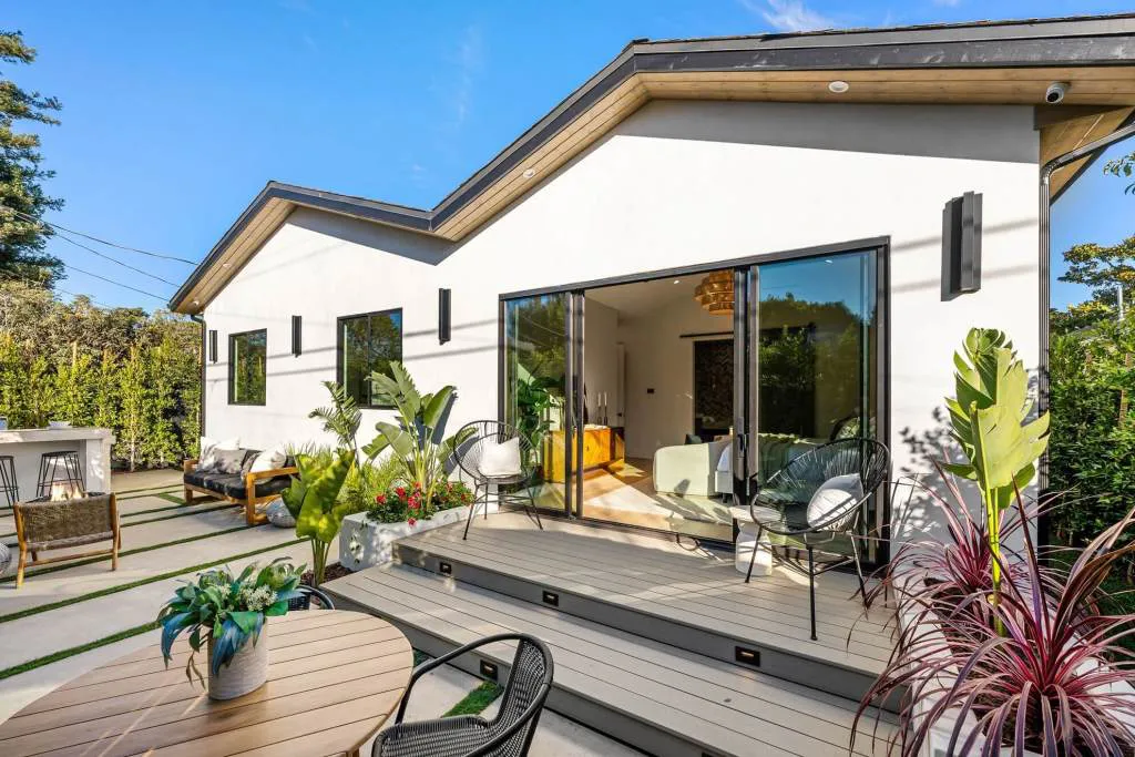 A modern home exterior with sliding doors leading to a patio, featuring outdoor seating and lush plants, designed by Mana Construction Inc. in Vallejo.