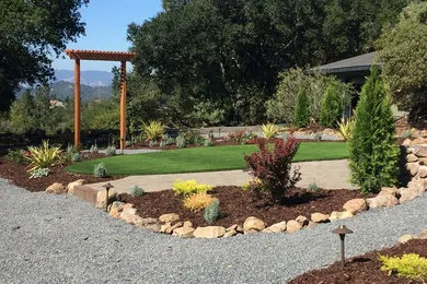 A landscaped garden with a manicured lawn, bordered by rocks and various plants, featuring a wooden archway, designed by Manzanita Landscape Construction, Inc. in Windsor.