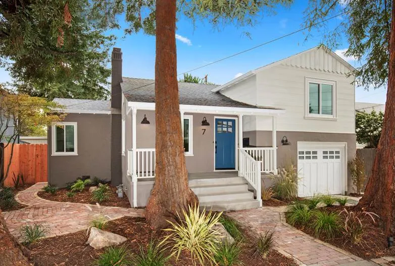 A charming house in Berkeley featuring a gray exterior, blue front door, and surrounding greenery, represented by the Marc Guay Team.