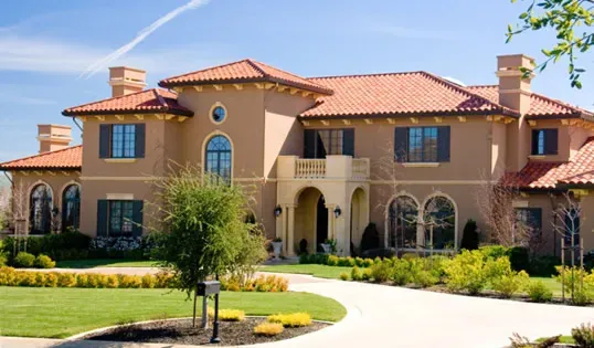 "A large, elegant house with a terracotta-tiled roof, well-manicured lawn, and surrounding greenery, showcasing Marco Roofing's work in Fremont."