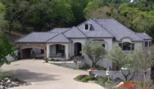 A large, elegant house with a gray roof surrounded by trees and landscaping, showcasing the work of Marco Roofing in Fremont.