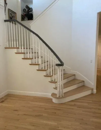 A wooden staircase with white railings and a dark handrail, designed by Martinez Stair Co. in Concord, featuring a curved structure and light wood flooring.
