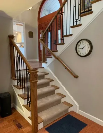 A staircase with wooden railings and carpeted steps in a home, with a wall clock on the side.