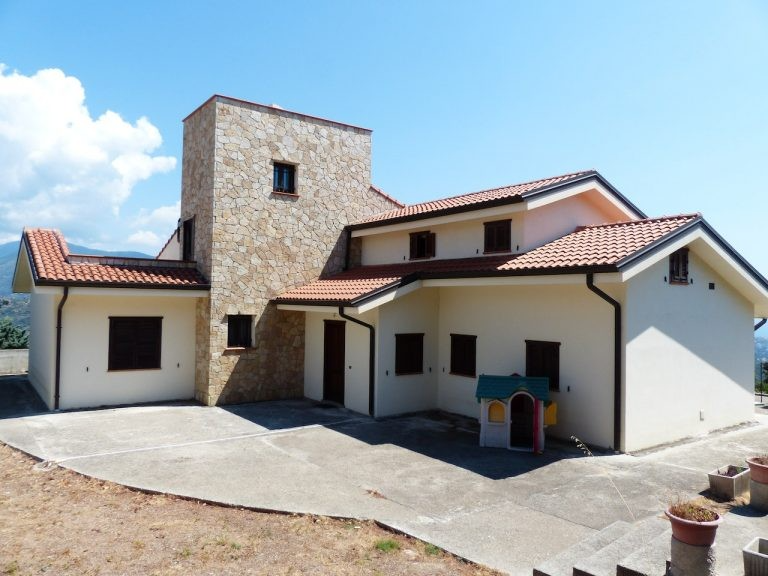 A newly constructed house in San Mateo featuring a blend of stone and stucco architecture, designed by Masterful Construction, with a prominent tower and a red-tiled roof.