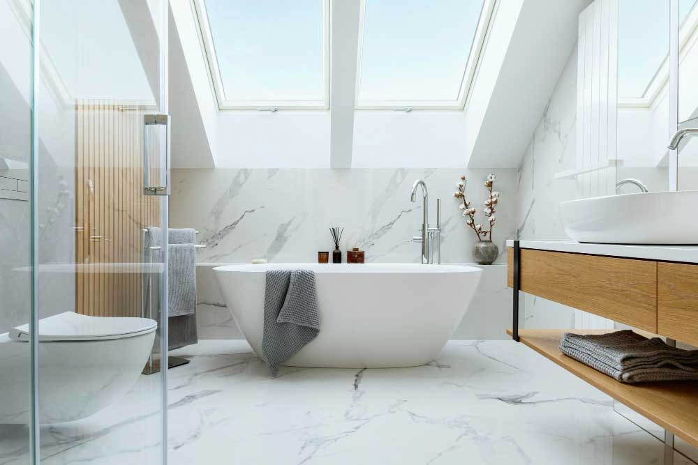 A spacious, modern bathroom in San Mateo with a large freestanding bathtub, marble flooring, wooden elements, and skylights, designed by Masterful Construction.