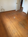 A room with hardwood flooring showing signs of wear, with an open door in the background, showcasing the potential for renovation by Mattie's Hardwood Flooring in Petaluma.