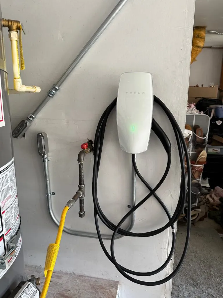 An electric vehicle charging station mounted on a wall in a garage, displaying a connected charging cable.