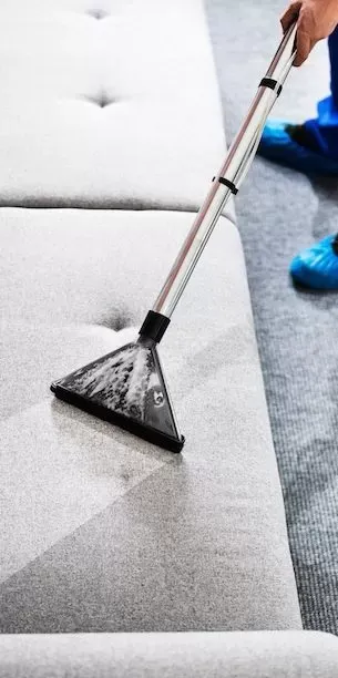 "A person using a vacuum cleaner on a gray upholstered surface, representing McHale's Environmental Insulation, Inc. in Concord, focusing on detailed upholstery cleaning."
