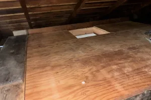 Image of a wooden attic floor with a cut-out section, showcasing insulation work by McHale's Environmental Insulation, Inc. in Concord.