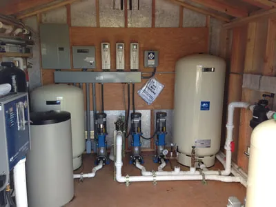 Interior of a water filtration system installation with tanks and pipes inside a wooden shed.