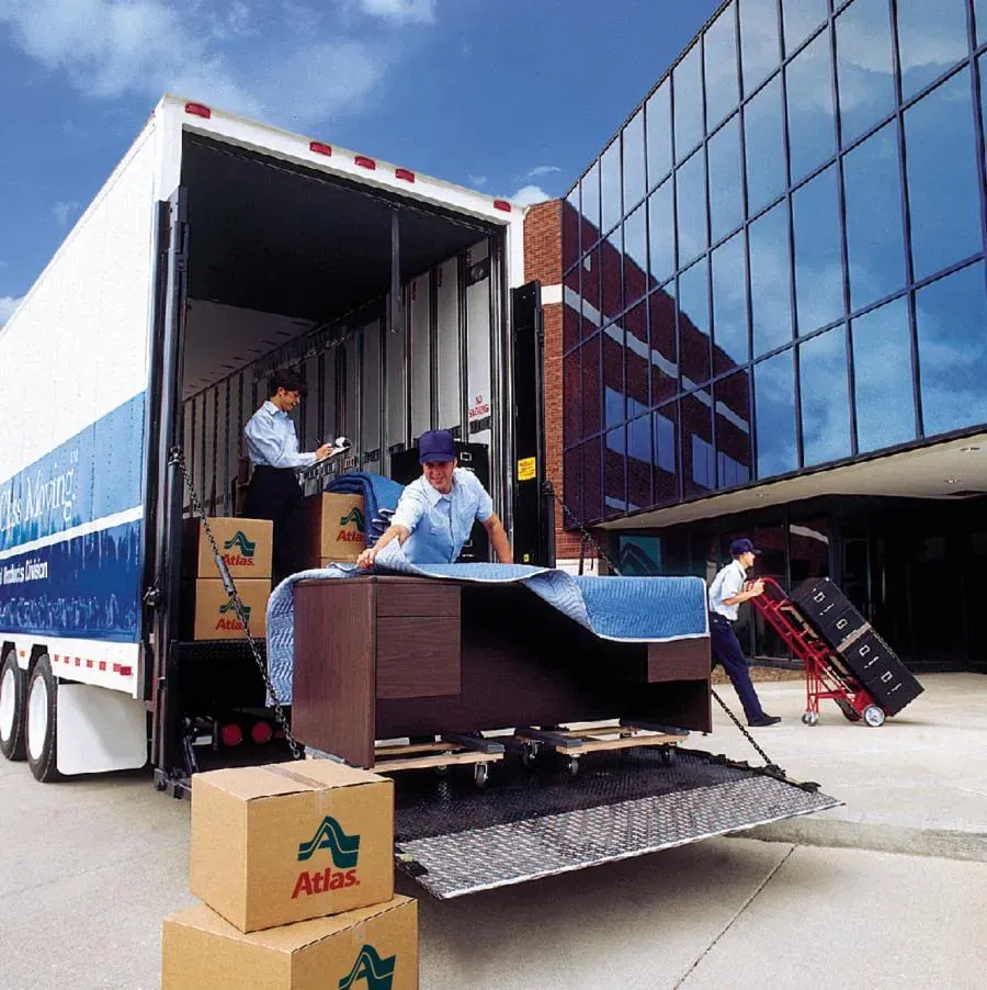 Moving team from Metropolitan Van & Storage, Inc. in Fairfield loading furniture and boxes into a moving truck outside a modern glass building.