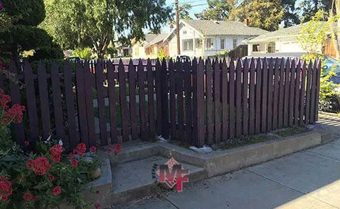 A purple wooden fence by Meza'sFence in San Jose, surrounding a residential garden with flowers and trees in the background.