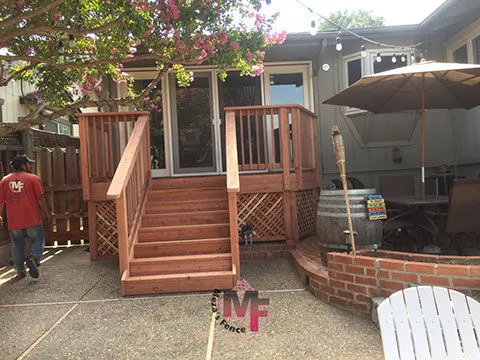 A wooden deck and stairs constructed by Meza'sFence in San Jose, featuring a patio with seating, lights, and a tree providing shade.