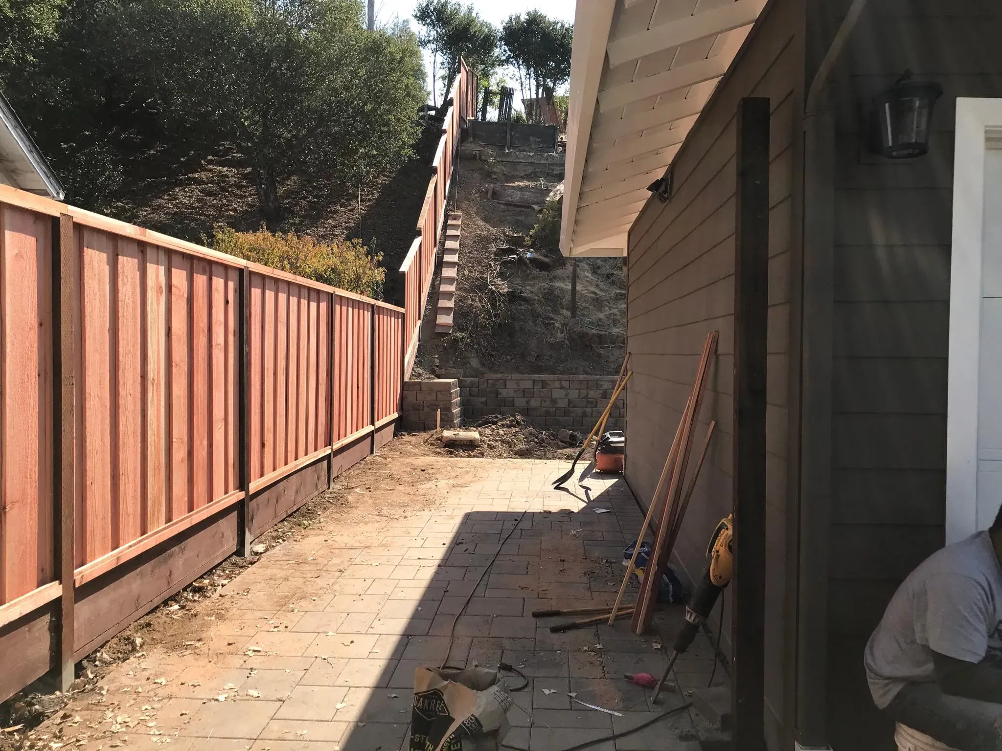 A newly installed wooden fence by Meza'sFence in San Jose, running alongside a house and yard, with construction tools visible on the ground.