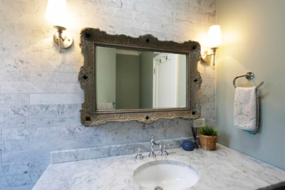 A bathroom with a large decorative mirror, marble countertop, sink, and two wall-mounted light fixtures on either side of the mirror.