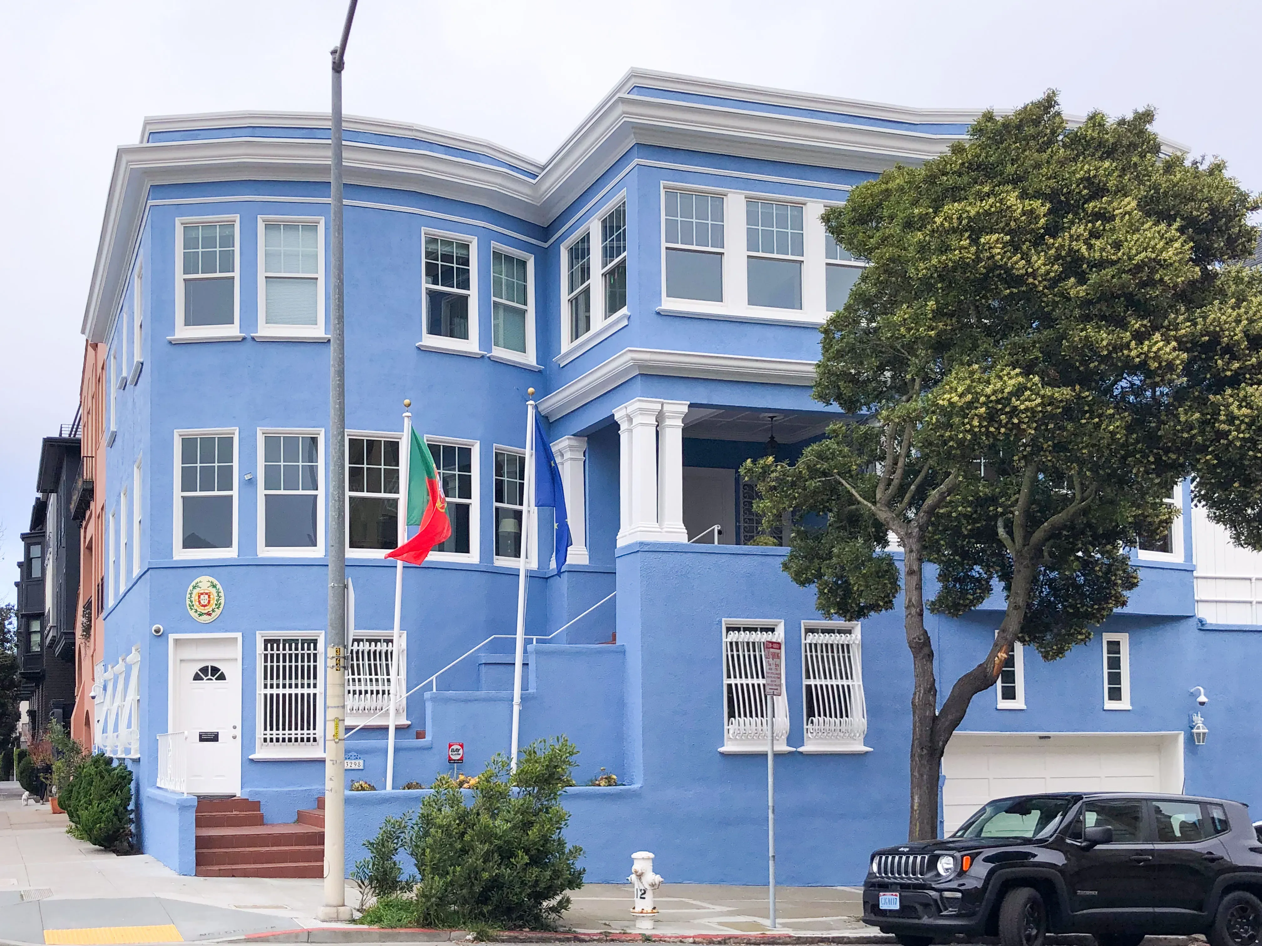 A large blue building in San Francisco with multiple windows, trees in front, and flags displayed, painted by Michael Sack Painting, Inc.