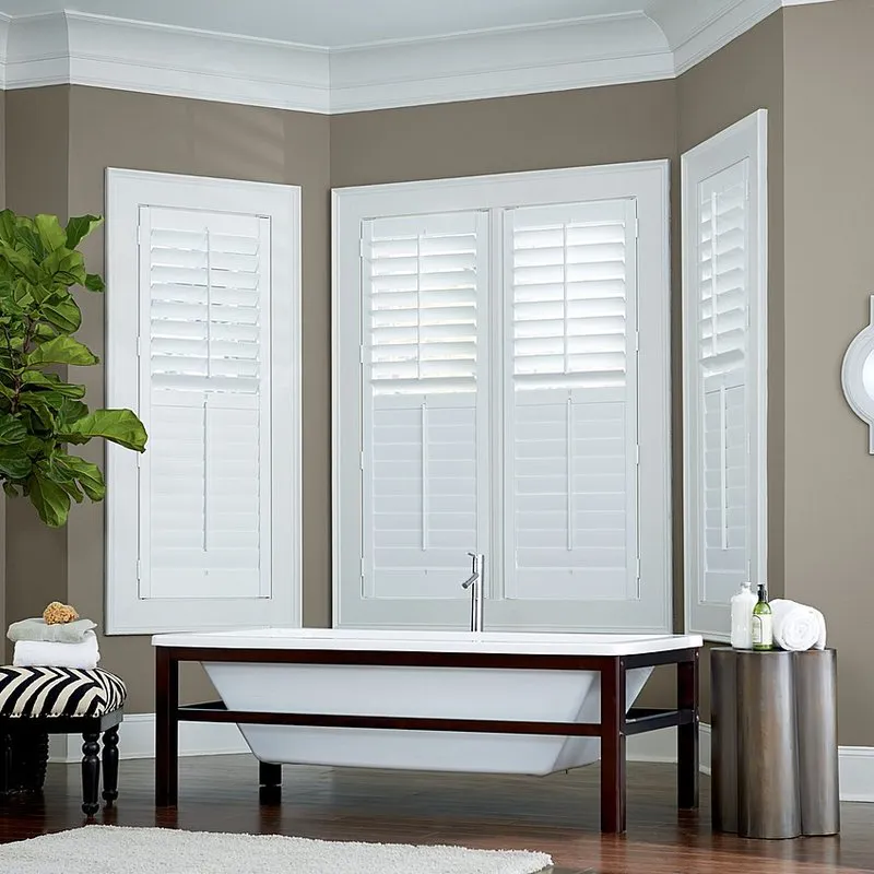 A bathroom with a freestanding tub, surrounded by windows fitted with white shutters, designed by Miller Window Covering in Novato.