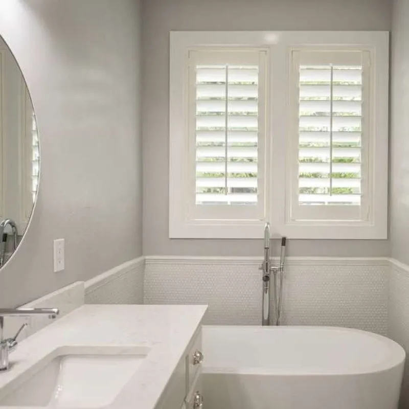 A bathroom featuring a bathtub and a window with white shutters, showcasing the work of Miller Window Covering in Novato.