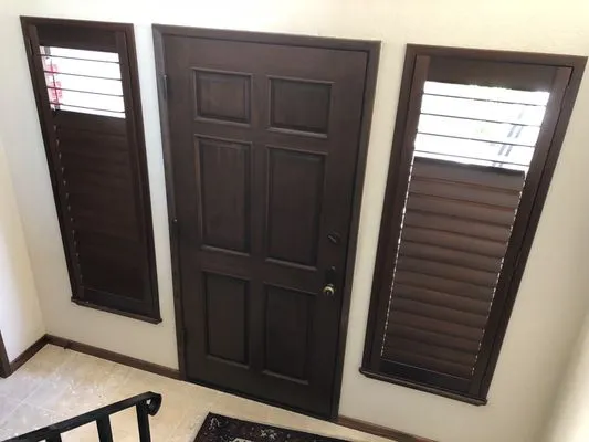 A front door flanked by two tall windows, each fitted with dark wooden shutters, providing privacy and aesthetic appeal in an entryway.