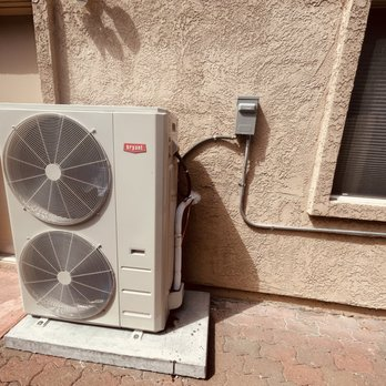 Outdoor heating and cooling unit installed on a concrete slab against a stucco wall in Gonzales.