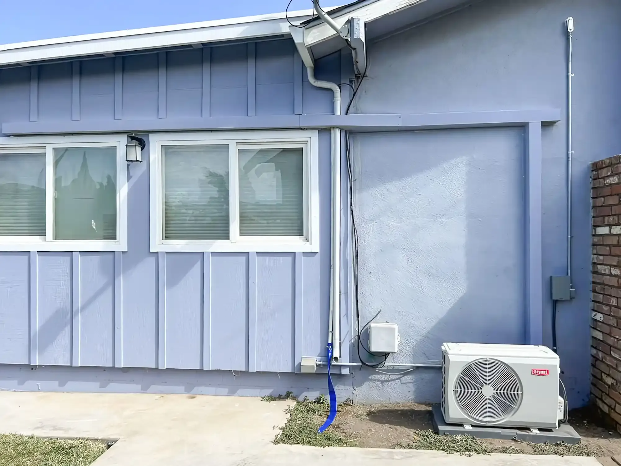 "Image of an outdoor air conditioning unit installed on the side of a blue house by Monterey Bay Heating and Cooling in Gonzales."