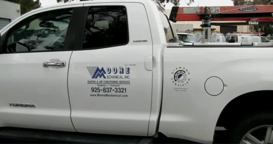 A white truck with the logo of Moore Mechanical Heating & Air Conditioning, featuring a ladder on top and parked outdoors in Dublin.