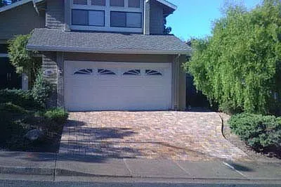 A well-constructed brick driveway leading to a garage in front of a house, surrounded by greenery, completed by Mr. Pavers Contractor Services, Inc. in Rodeo.
