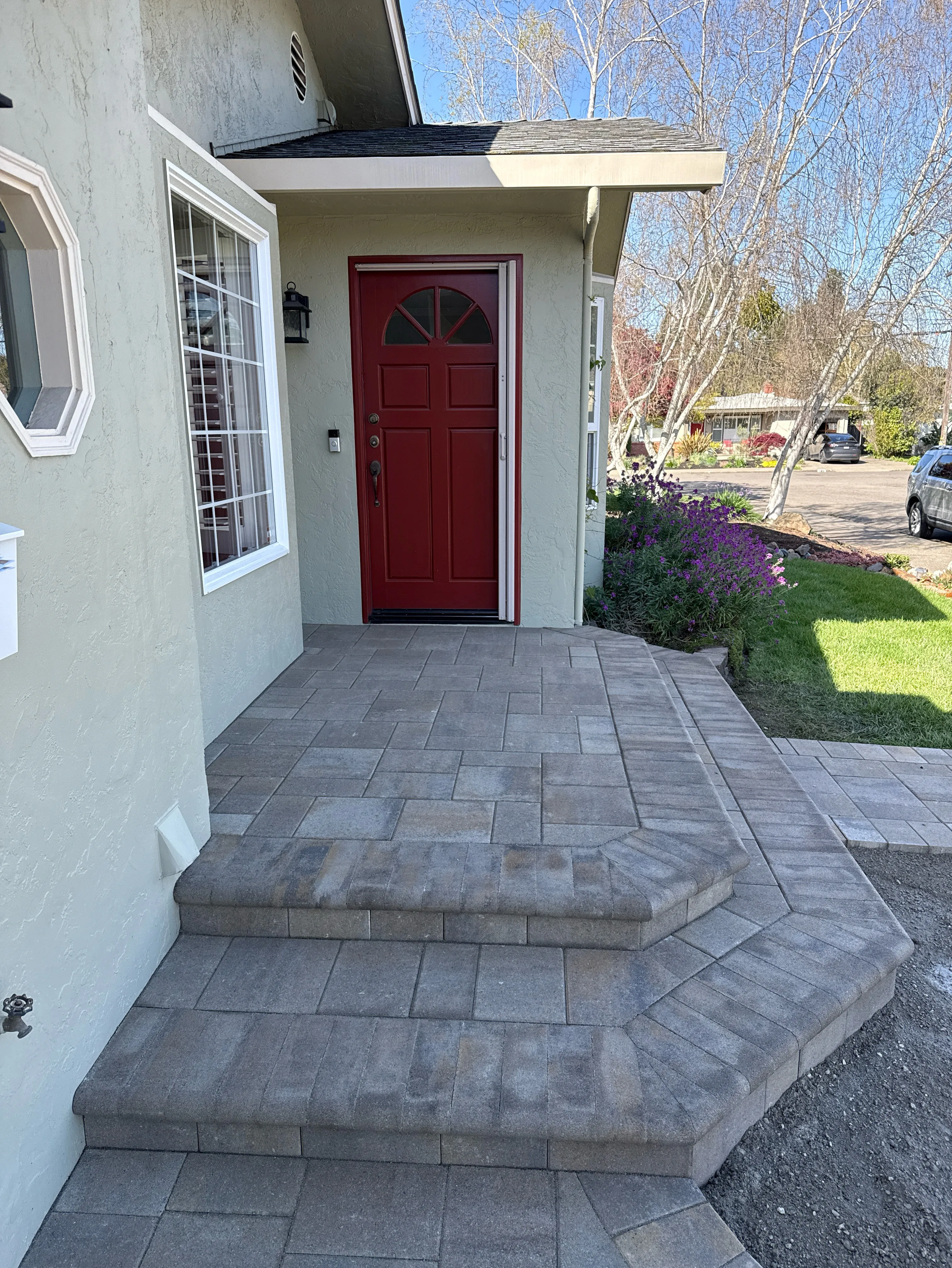 A front porch with gray stone pavers and steps, leading to a red door, completed by Mr. Pavers Contractor Services, Inc. in Rodeo.
