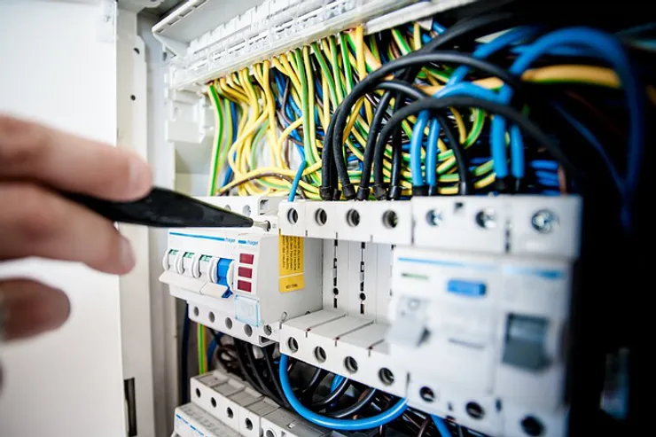 A close-up of an electrical panel with various colored wires and switches, with a hand using a tool for adjustments.