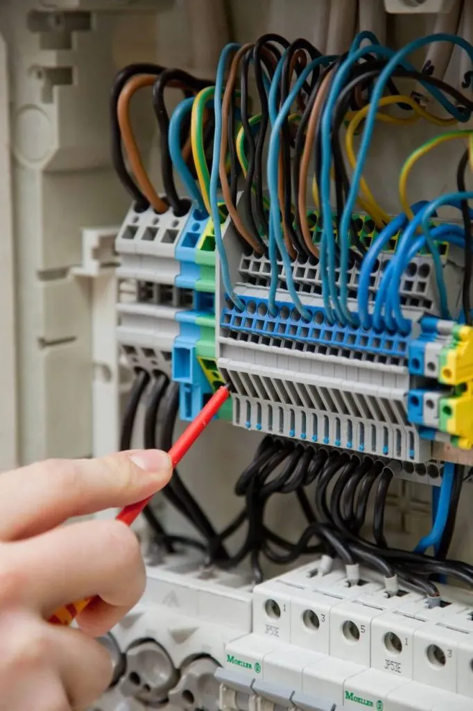 A hand using a red tool to interact with a complex electrical panel containing multiple colored wires.