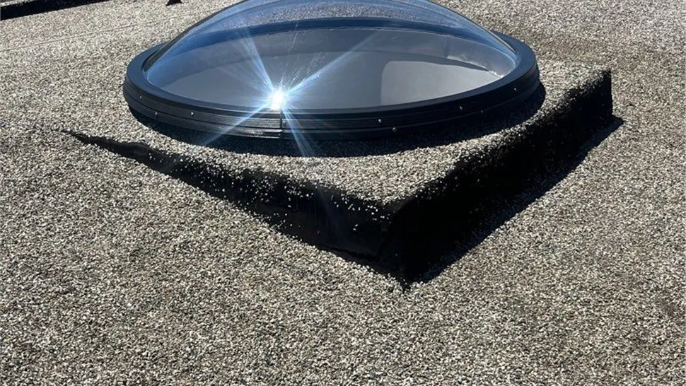 "A dome-shaped skylight installed on a gravel-covered flat roof, reflecting sunlight, showcasing the craftsmanship of Mr. Roofing, Inc. in South San Francisco."