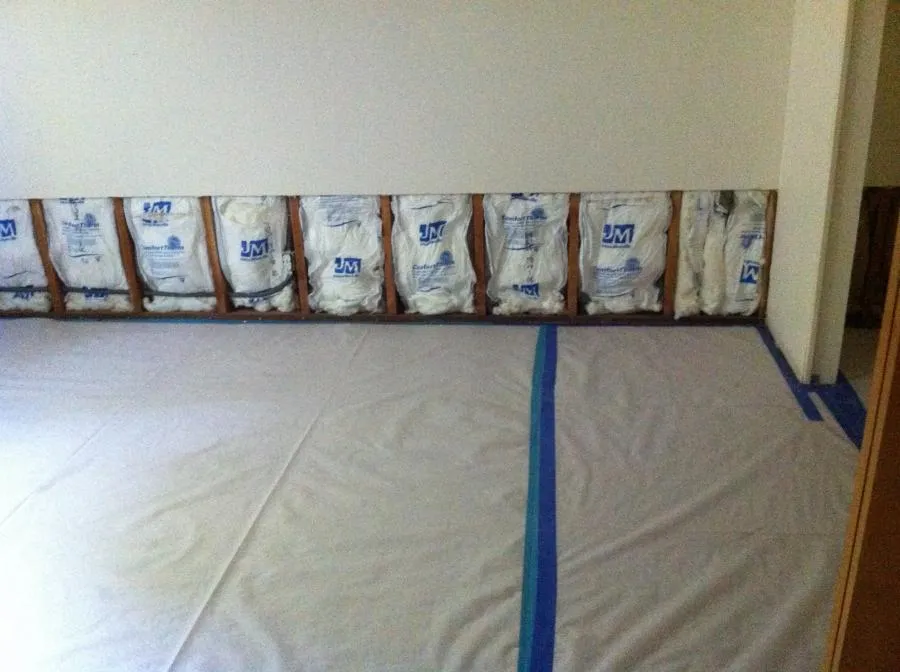 Interior view of a partially renovated room showing exposed wall insulation and a protective floor covering by NBE Property Restoration in Santa Rosa.