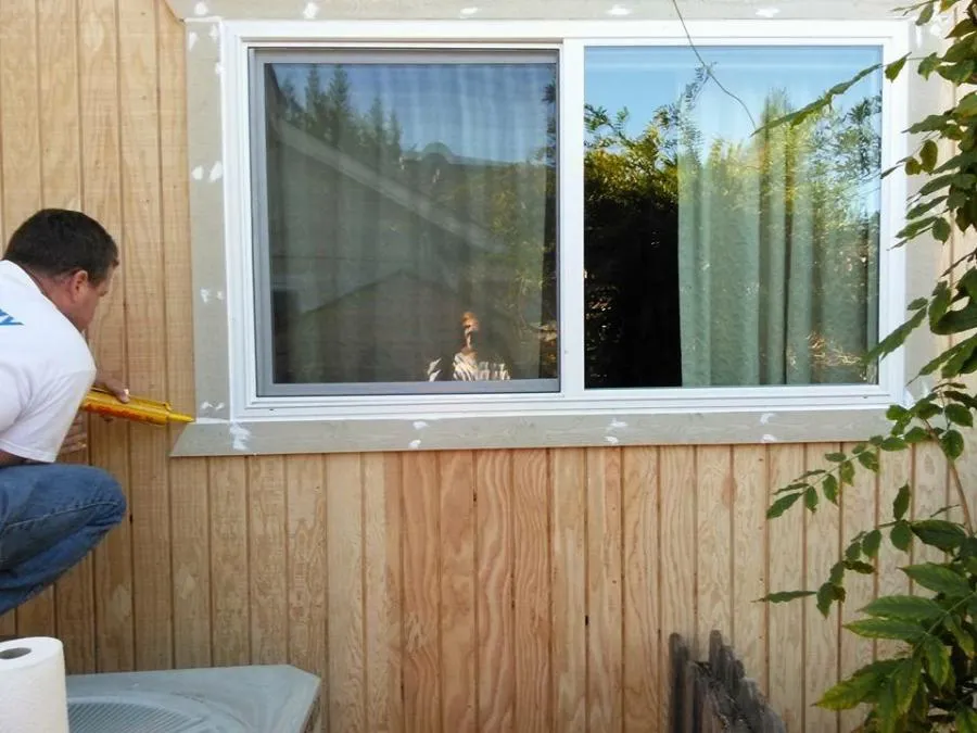 "A professional from NBE Property Restoration applies caulking around a window frame on a wooden exterior wall in Santa Rosa."