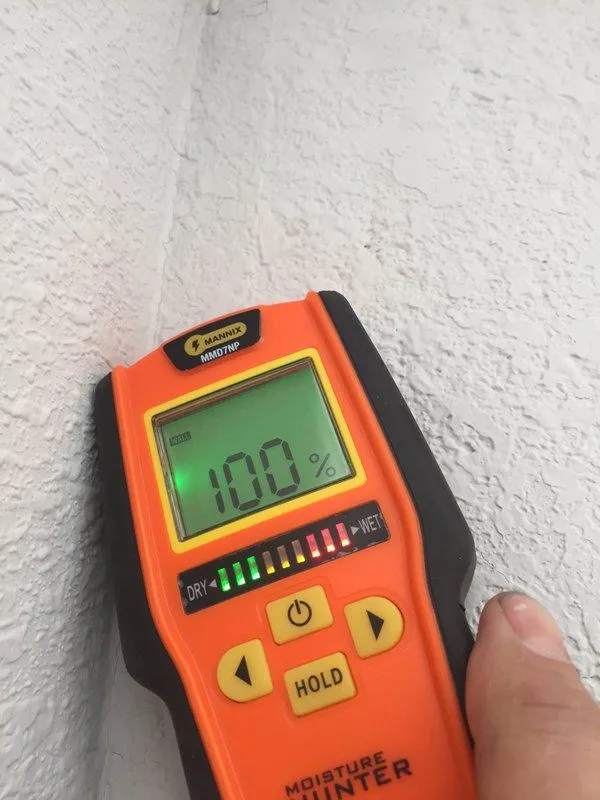 "A digital moisture meter displaying a 100% reading against a textured wall, used by NBE Property Restoration in Santa Rosa."