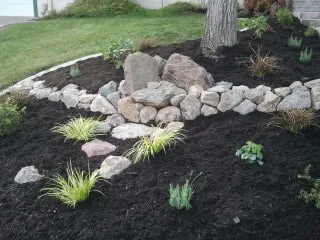 A landscaped garden in Concord with neatly arranged rocks, various plants, and mulch, designed by Natural Landscaping Contractors.