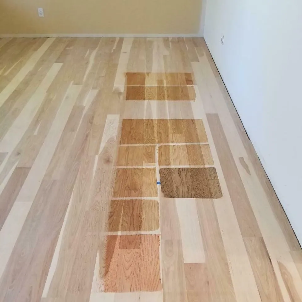 A range of wood floor stain samples are displayed on a light hardwood floor, showcasing various shades and finishes by Navarro Flooring in Rohnert Park.