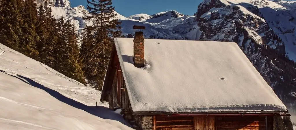 A snow-covered cabin in a mountainous landscape, illustrating the importance of effective roofing in harsh conditions.