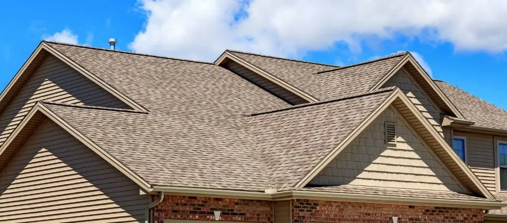 A detailed image of a house showing a complex, multi-gabled roof with brown shingles against a blue sky, representing the craftsmanship of New Era Roofing, LLC in Sacramento.