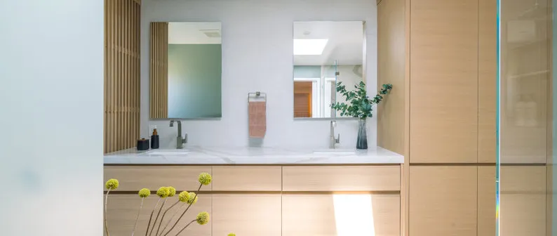 A modern bathroom interior featuring dual sinks with mirrors, wooden cabinetry, and minimalist decor, designed by Next Stage Design + Build in San Jose.